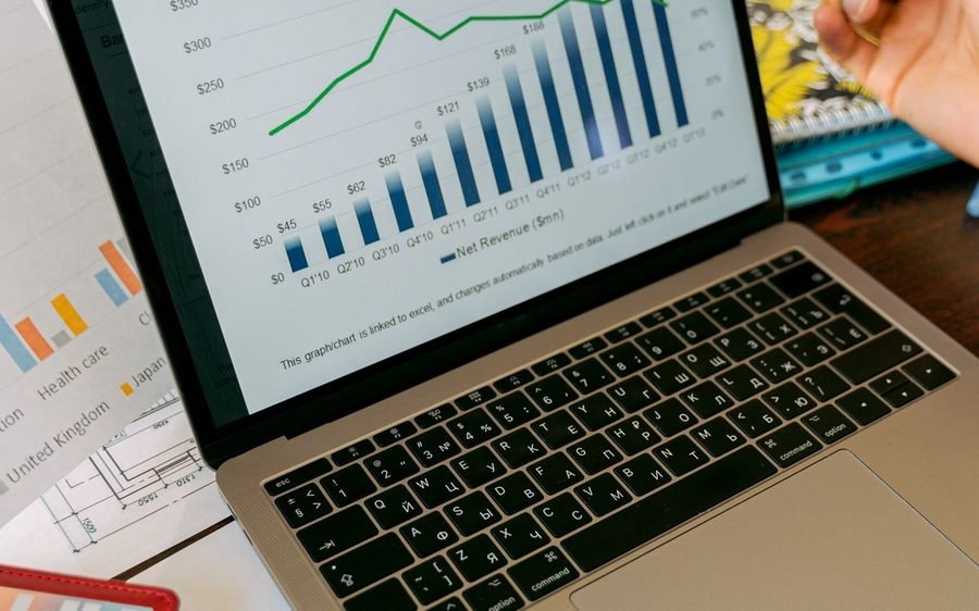 Laptop showing a business performance chart beside printed reports